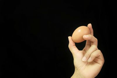 Close-up of hand holding apple against black background