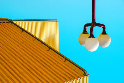 Lamp hanging by house roof against clear blue sky