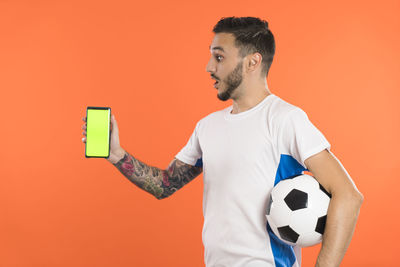 Low angle view of man holding ball against orange background