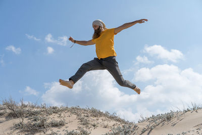 Carefree man with arms outstretched jumping on sand at beach