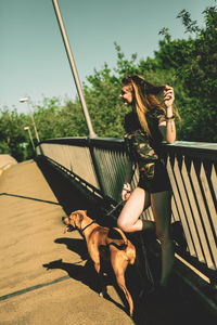 Woman standing by dog on footpath while leaning on railing