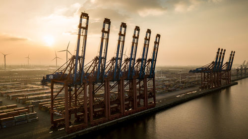 Machineries at dock against sky during sunset