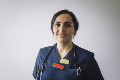 Portrait of smiling female healthcare worker against white wall