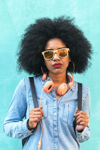 Portrait of young woman wearing sunglasses standing against blue wall