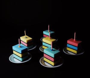 Close-up of candles over multi colored sponge stacked in plate against black background