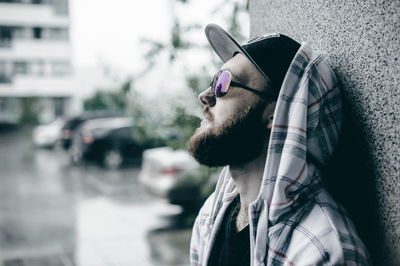 Young man smoking while standing by wall during rain