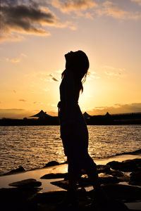 Silhouette woman standing at beach against sky during sunset