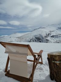 Chairs and tables on snow covered land against sky