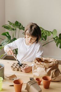 A cute little girl is planting or transplanting plants in a flower pot at home. hobby for children 