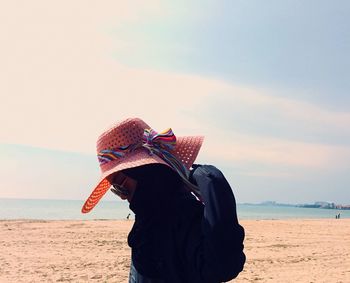 Teenage girl wearing hat while standing at beach against sky