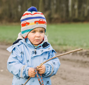 Cute girl wearing warm clothing while holding stick outdoors