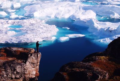 Man standing on cliff against icebergs in sea