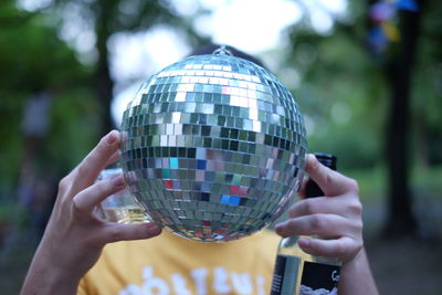 Close-up of man holding disco ball in front of face with alcohol bottle