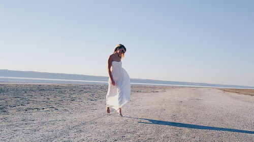 Full length of woman standing on beach against clear sky