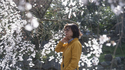 Side view of young woman standing against trees