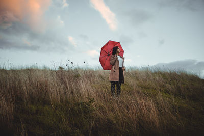 Woman holding umbrella on field against sky