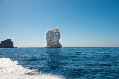 Rock formation in sea against clear blue sky