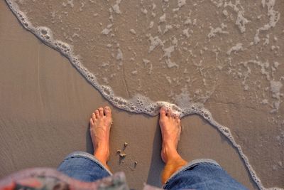 Low section of man standing on wet shore