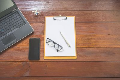 Close-up high angle view of laptop and smart phone with paper on wooden table