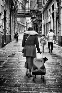 Rear view of woman with luggage on street amidst buildings