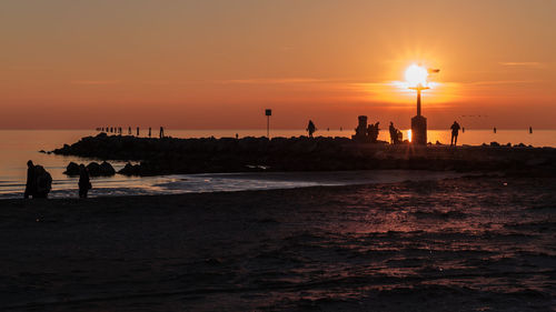 Silhouette people on beach against sky during sunset