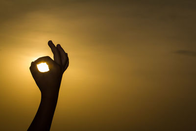 Close-up of silhouette hand against sky during sunset