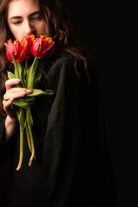 Close-up of young woman holding rose against black background