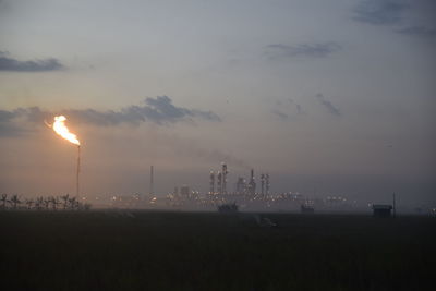 Burning flare stack and industrial buildings against sky during sunset , 