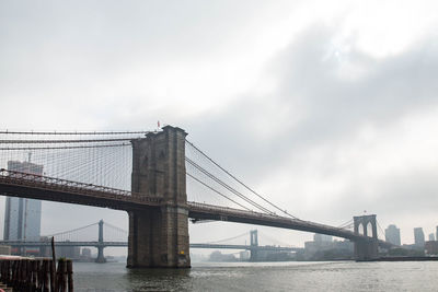 Suspension bridge over river against cloudy sky