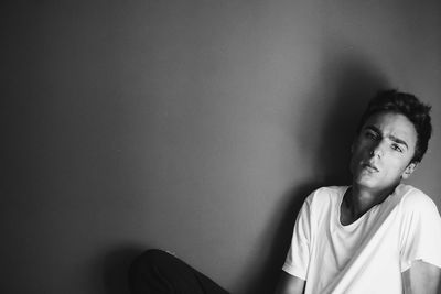 Portrait of young man sitting against wall at home