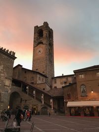 People walking on street by buildings against sky during sunset