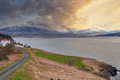 Scenic view of road on grassy hill by seascape against mountain during sunset