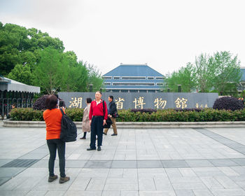 Rear view of people walking by building against sky