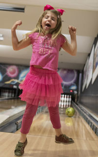 Full length of happy girl jumping on bowling alley