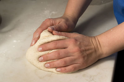 Cropped hands kneading dough on table