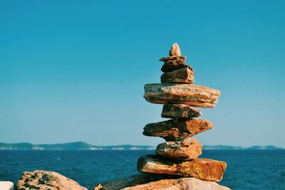 Stack of stones by sea against blue sky