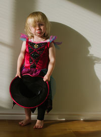 Portrait of sad girl in costume holding hat while standing against wall at home