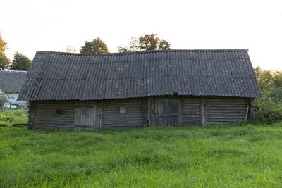 Barn on grassy field by houses against sky