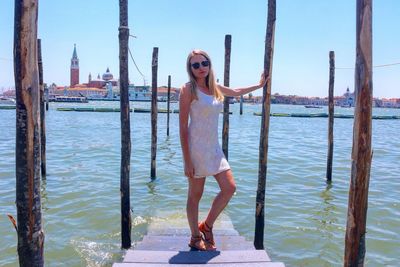 Portrait of young woman standing on pier by grand canal against sky
