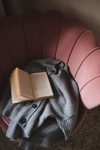 Open paper book with knitted wool fabric on cozy accent chair in room close up.