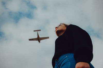 Low section of woman standing against airplane flying in sky