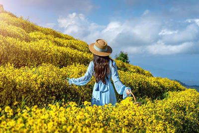 Rear view of woman standing on field against cloudy sky