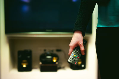 Midsection of woman holding remote control while standing at home