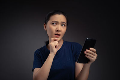 Portrait of young woman using mobile phone against black background