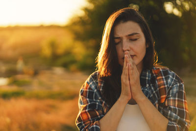 Woman closed her eyes, praying in a field during beautiful sunset.