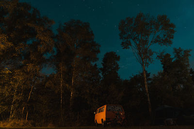 Orange van in front of trees growing on field against sky at night