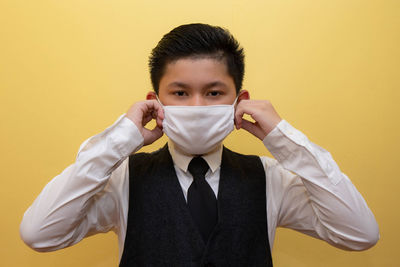 Portrait of young man standing against yellow background