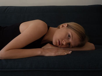 Beautiful caucasian young female natural model tired looking to camera resting on dark green sofa