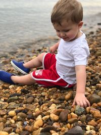 Side view of boy sitting on stones at sea shore