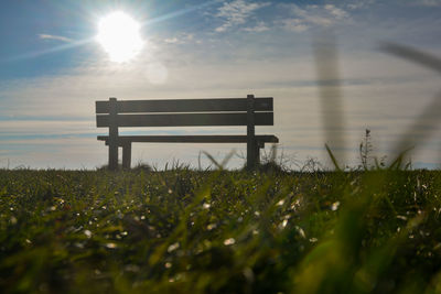 Empty bench on field against sky